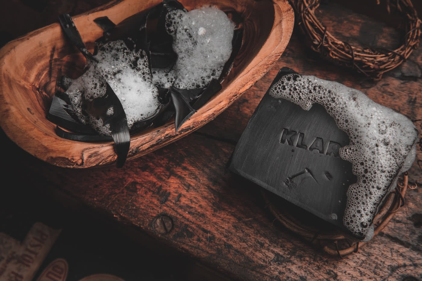 Charcoal soap lathering in a wooden bowl beside a second embossed Klarif bar
